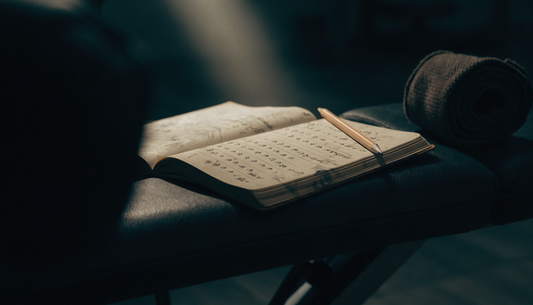 Aufgeschlagenes Notizbuch mit handschriftlichen Trainingszahlen auf einer Hantelbank