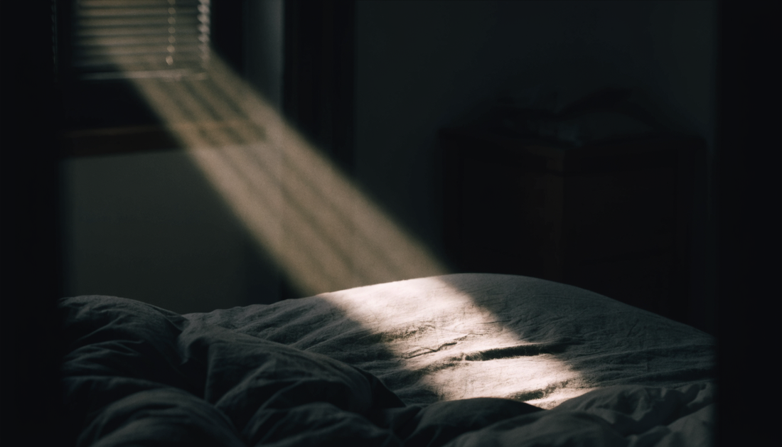 Dunkles Schlafzimmer im Morgengrauen, ein Lichtstreifen faellt durch die Jalousie