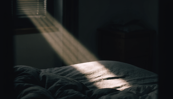 Dunkles Schlafzimmer im Morgengrauen, ein Lichtstreifen faellt durch die Jalousie